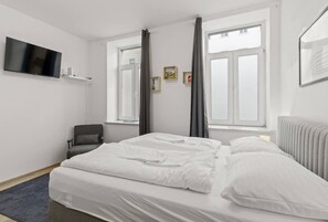 Een hotelkamer met een bed, een stoel, een televisie en een raam met gordijnen.