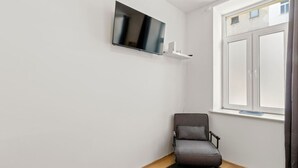 A corner room with a flat-screen TV mounted on the wall, a chair, and a window with curtains. - FarawayHomes Studio Vienna #3 (Vienna)