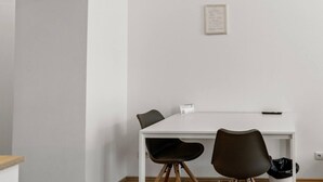 A minimalist room with a white table, two chairs, a framed certificate on the wall, and a trash bin. - FarawayHomes Studio Vienna #3 (Vienna)