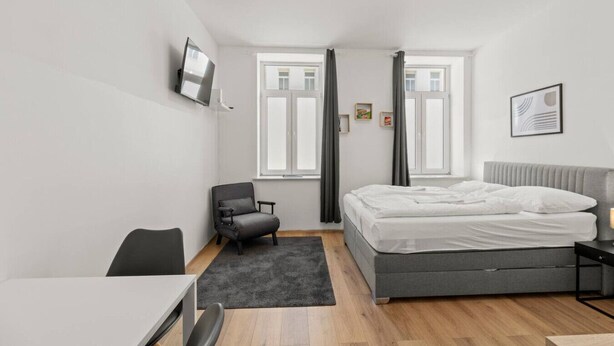 A modern bedroom with a bed, a desk, a chair, and a TV on the wall. - FarawayHomes Studio Vienna #3 (Vienna)