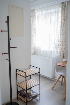 Ett rum med ett vitt element, ett träbord med en vit stol, en svart metallhylla och ett fönster med blommiga gardiner.
