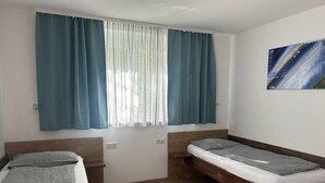 A room with two wooden beds, a window with curtains, a wall-mounted artwork, and a light switch. - FarawayHomes Aparthotel Kremsmünster #22 (Kremsmünster)