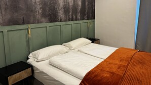 Un lit avec du linge de lit blanc, une tête de lit verte et un plaid marron.