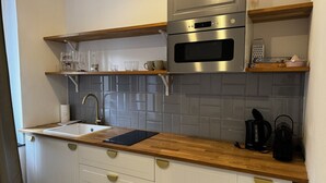 Une cuisine de taille réduite avec des meubles blancs, un plan de travail en bois, un four en acier inoxydable et une machine à café.