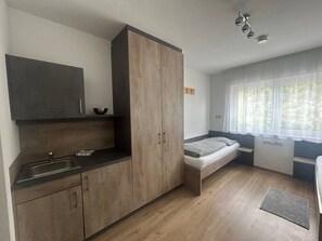 A compact room with a kitchenette, a bed, and a window with sheer curtains.