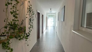 A hallway with tiled flooring, white walls, and a hanging plant. - FarawayHomes Aparthotel Kremsmünster #25 (Kremsmünster)