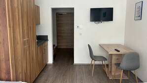 A compact room with a kitchenette, a TV mounted on the wall, and a desk with two chairs. - FarawayHomes Aparthotel Kremsmünster #25 (Kremsmünster)
