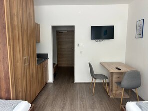 Ein kompaktes Zimmer mit Küchenzeile, einem an der Wand befestigten Fernseher und einem Schreibtisch mit zwei Stühlen.