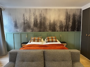 A bedroom with a bed, green wardrobe, and a forest mural on the wall.