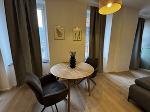 A room with a round wooden table, two chairs, a potted plant, and framed artwork on the wall.