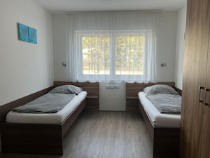 Ein Zimmer mit zwei Einzelbetten, einem kleinen Tisch und einem Fenster mit Vorhängen.