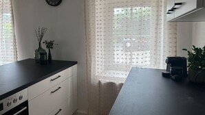 Eine Küche mit einer Uhr, einem Fenster mit gemusterten Vorhängen und einer Kaffeemaschine.