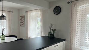 Eine Küche mit schwarzer Arbeitsplatte, weißen Schränken, einer Uhr und einem Fenster mit gemusterten Vorhängen.