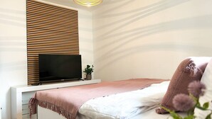 Ein modernes Schlafzimmer mit Bett, Fernseher, Pflanze und einem außergewöhnlichen Wanddesign.