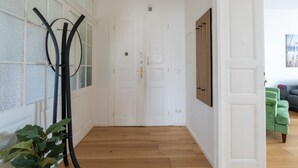 Un corridoio con pavimento in legno, porte bianche e un divano verde sullo sfondo.