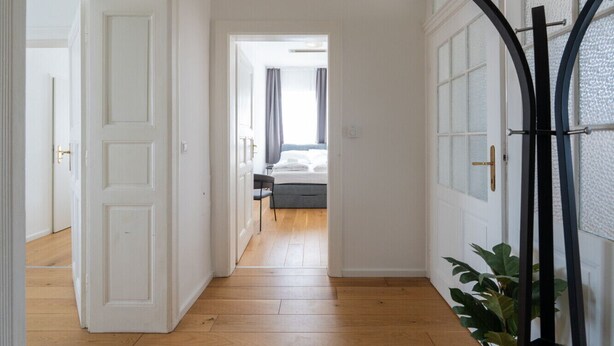 Un corridoio con pavimento in legno che conduce a una camera da letto con un letto e una sedia.