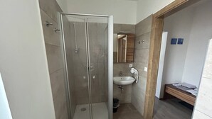 A bathroom with a glass-enclosed shower, a sink, and a wooden bench. - FarawayHomes Aparthotel Kremsmünster #13 (Kremsmünster)