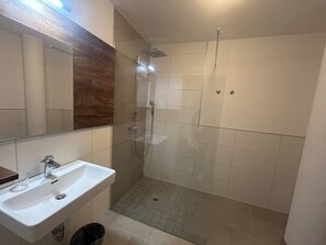 Un baño con lavamanos blanco, un espejo y cabina de ducha con paredes de vidrio.