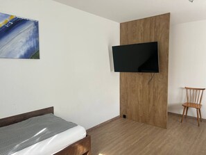 Ein Schlafzimmer mit einem Bett, einem an einer Holzplatte montierten Fernseher und einem Sessel.
