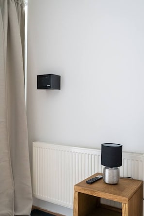Une chambre avec un thermostat fixé au mur, une table de chevet avec une lampe et un radiateur.