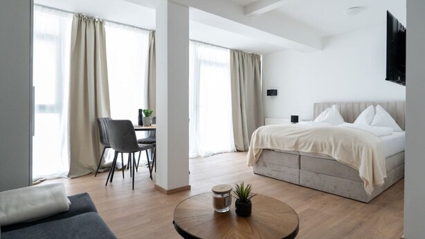 A modern hotel room with a bed, a desk, a chair, a round table, and a TV.