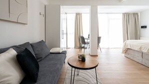 A modern, well-lit room with a grey sofa, a round coffee table, and a bed.