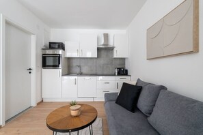 Uma cozinha moderna com armários brancos, forno embutido e bancada cinza.