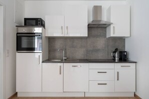 Eine moderne Küche mit weißen Schränken, einem Edelstahlbackofen, einer Mikrowelle, einem Spülbecken und einer Kaffeemaschine.
