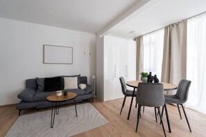 Ein modernes Wohnzimmer mit einem grauen Sofa, einem runden Couchtisch und einem Esstisch mit Stühlen.
