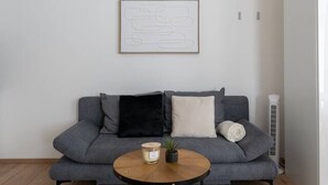 Ett modernt vardagsrum med en grå soffa, ett runt soffbord i trä och en grå matta.