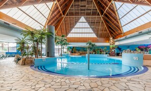 An indoor swimming pool with a stone-tiled floor, wooden beams, and tropical plants. - Stunning Bungalow With Pool for 6 (Branville)