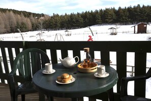 Ein Tisch mit Teekanne, Tassen und Keksen auf einer Terrasse mit Blick auf eine verschneite Landschaft.