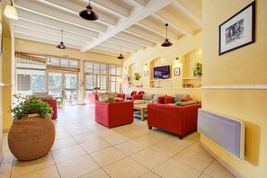 Eine geräumige Lobby mit roten Sofas, einem großen Kübelpflanzen, einem Fernseher und einem gerahmten Bild an der Wand.