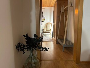 Ein Flur mit Holzboden, einem Sessel, einer Leiter und einer Vase mit dunklem Grünzeug.