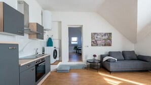 Una cocina moderna con horno empotrado, lavadora y comedor con sofá gris y una mesa pequeña.