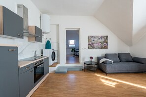 A modern kitchen with a built-in oven, a washing machine, and a dining area with a gray sofa and a small table.