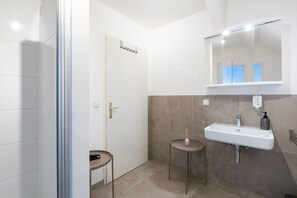 A bathroom with a shower, a sink, a mirror, and a small table.