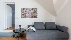Una sala de estar moderna con un sofá gris, una mesita redonda con un florero y un cuadro de colores sobre el sofá.