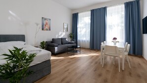 Una habitación moderna con cama, sofá, mesa de comedor con sillas y ventanas grandes con cortinas.