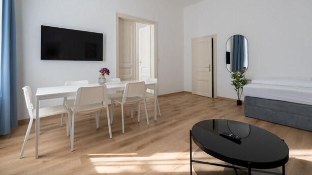 Una habitación moderna con una mesa de comedor, sillas, televisor, cama, espejo y una mesita con un control remoto.