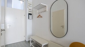 Una habitación con una puerta blanca, un banco, un espejo y un radiador.