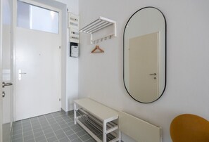 Une pièce avec une porte blanche, un banc, un miroir et un radiateur.