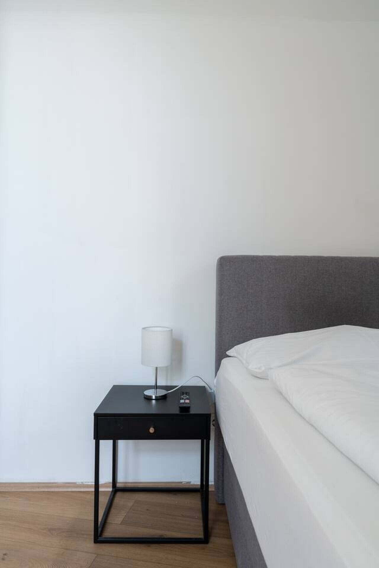 A minimalist bedroom with a bed, a nightstand with a lamp, and a power outlet.