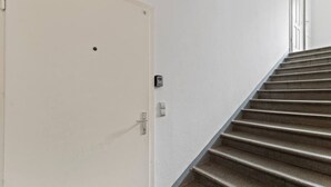 En trappa som leder upp till en vit dörr med ett nummer på, en dörrklocka och en ljusströmbrytare.