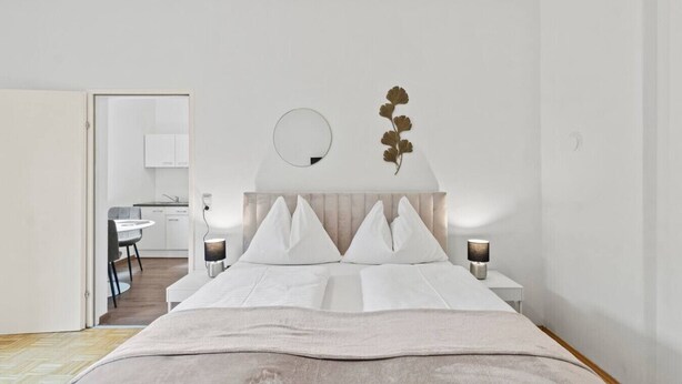 Ett modernt hotellrum med en säng, sänglampor, en rund spegel och en dekorativ väggdekoration.