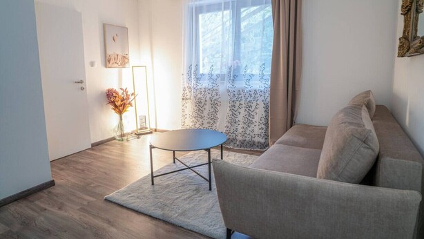 Uma sala de estar com sofá, mesa redonda, abajur e janela com cortinas.