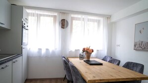 Uma cozinha moderna com mesa de jantar de madeira, cadeiras estofadas em cinza e um vaso com flores.