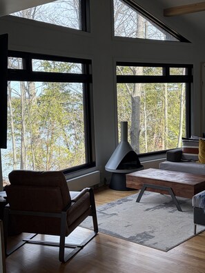 A modern living room with large windows, a fireplace, and a sofa. - Sunset View Retreat on Lake Champlain (Alburgh)