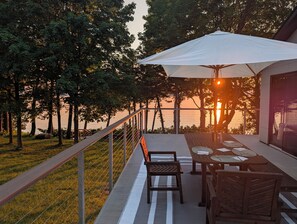 An outdoor seating area with a table and chairs, a railing, and a view of the sunset over the water. - Sunset View Retreat on Lake Champlain (Alburgh)