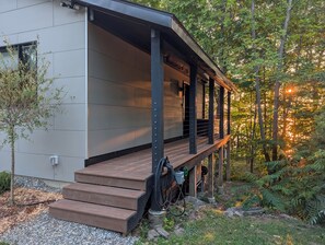 Moderni rakennus, jossa on katettu kuisti, ulkona sijaitsevat sähkölaitteet ja luonnonmukainen metsä taustalla.